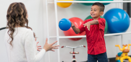 young boy throwing therapy ball to therapist, smiling