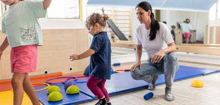 Therapist with children completing balance beam in therapy gym