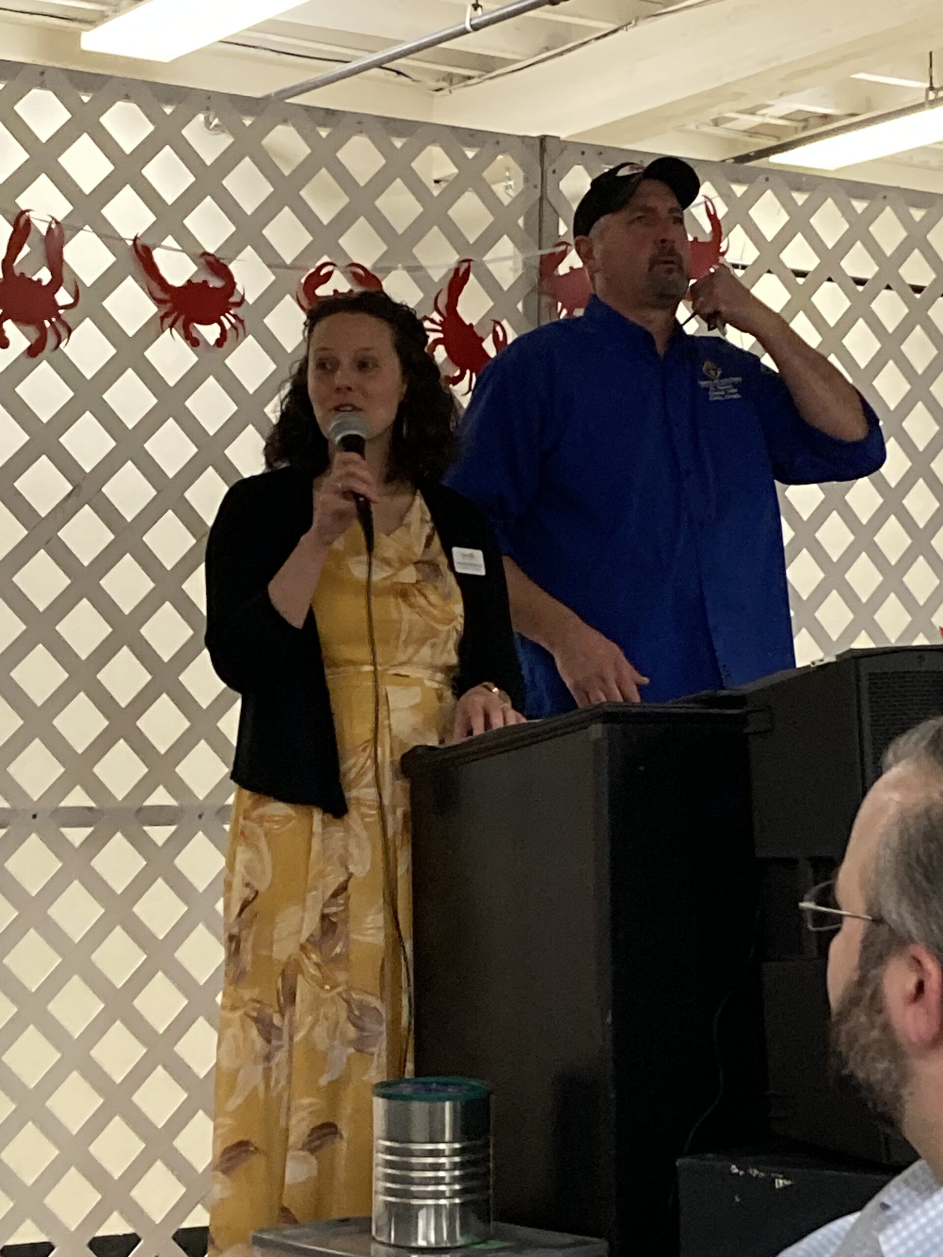 Neuro's Executive Director speaks into a microphone while delivering a passionate speech about Neuro and what we do as she stands next to Canby Knights of Columbus' Mike Schmader as they stand on a stage behind a podium.