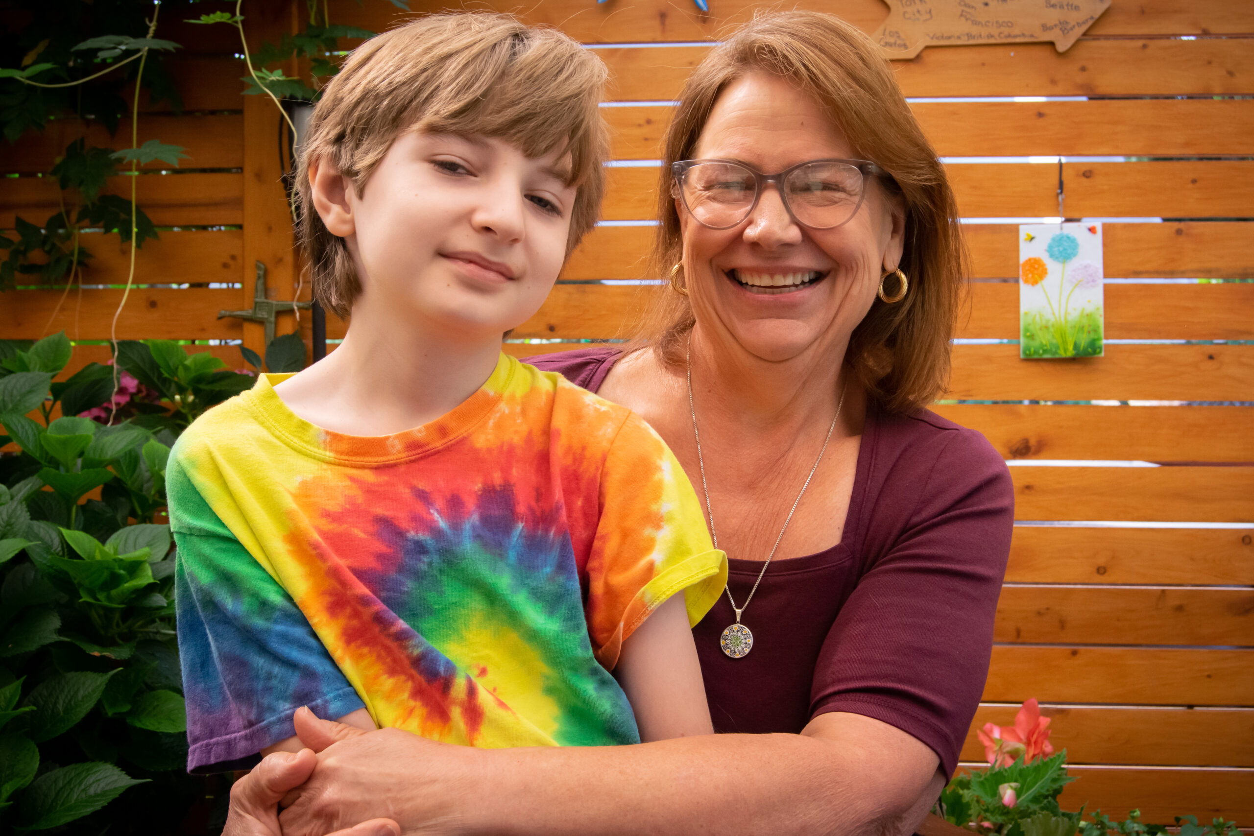 A photo of one of our families: Lisa and her child David, as he sits on her lap. Both are smiling and posing for the camera as they sit in front of their fence in their backyard.